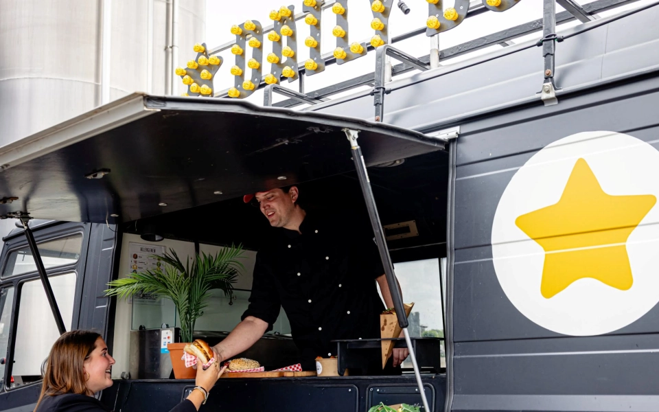Daily Dog kok reikt klant een gourmet hotdog aan